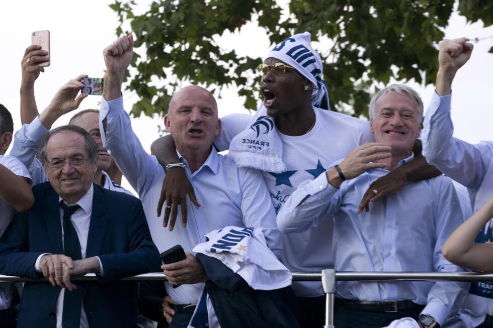 Le sélectionneur de l'équipe de France de football, Didier Deschamps (à droite), son adjoint Guy Stéphan (à gauche), le président de la Fédération Française de Football, Noël Le Graët, et le footballeur français Paul Pogba saluent la foule depuis le toit d'un bus lors du défilé sur la célèbre avenue des Champs-Élysées à Paris, le lundi 16 juillet 2018.